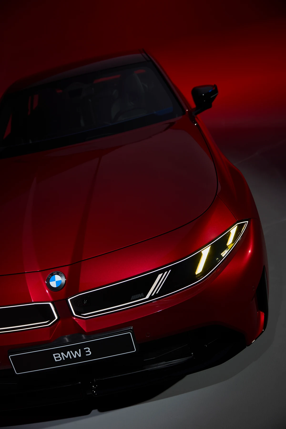 Close view of the red BMW 3 Series front end, including its hood badge, grille and illuminated headlamp graphic.