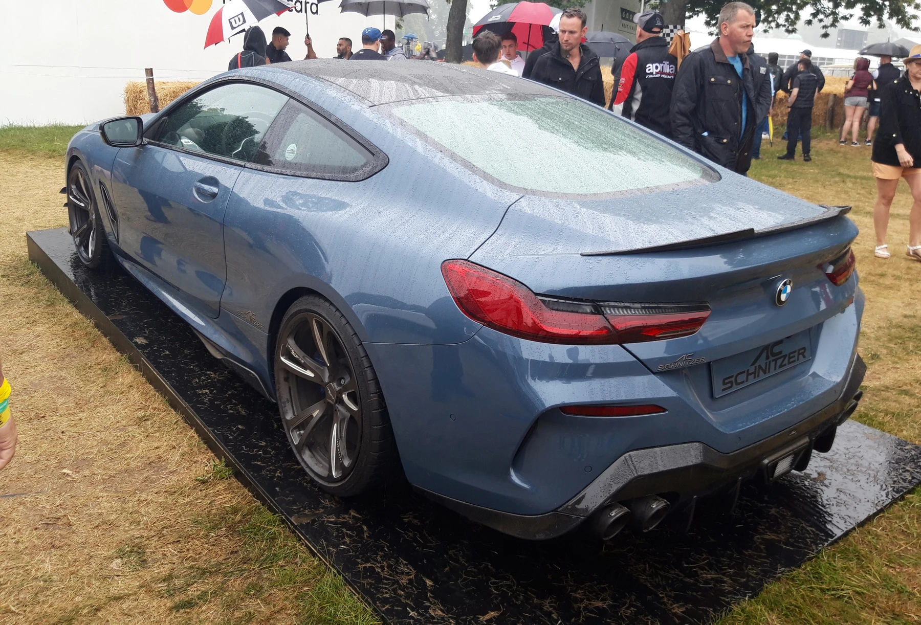 A blue AC Schnitzer ACS8 viewed from the rear three-quarter angle on the wet Goodwood Festival of Speed display area, with visitors behind it.